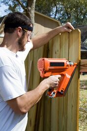 Picture of a man in a white shirt using a nail gun to put up a wood fence