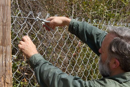 Picture of a man in a green shirt installing a chain link fence